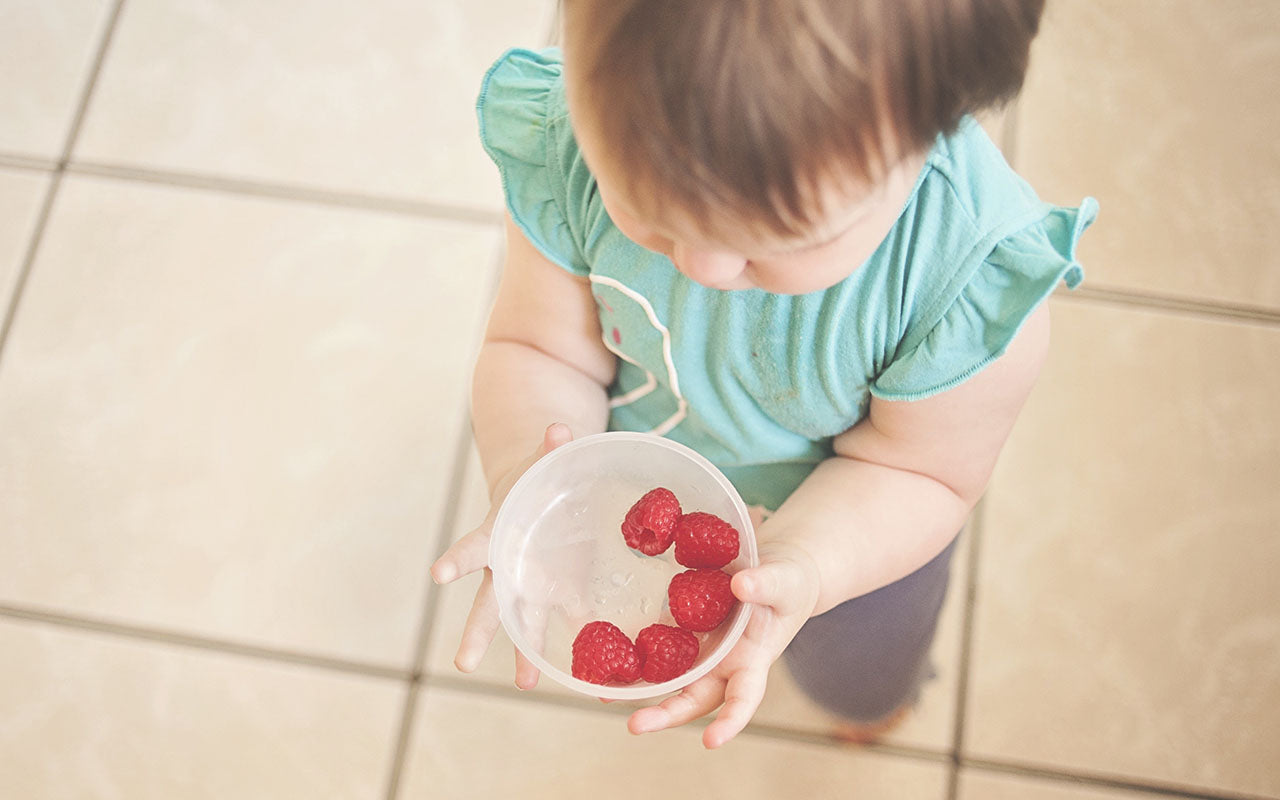 baby girl holding bowl of raspberries